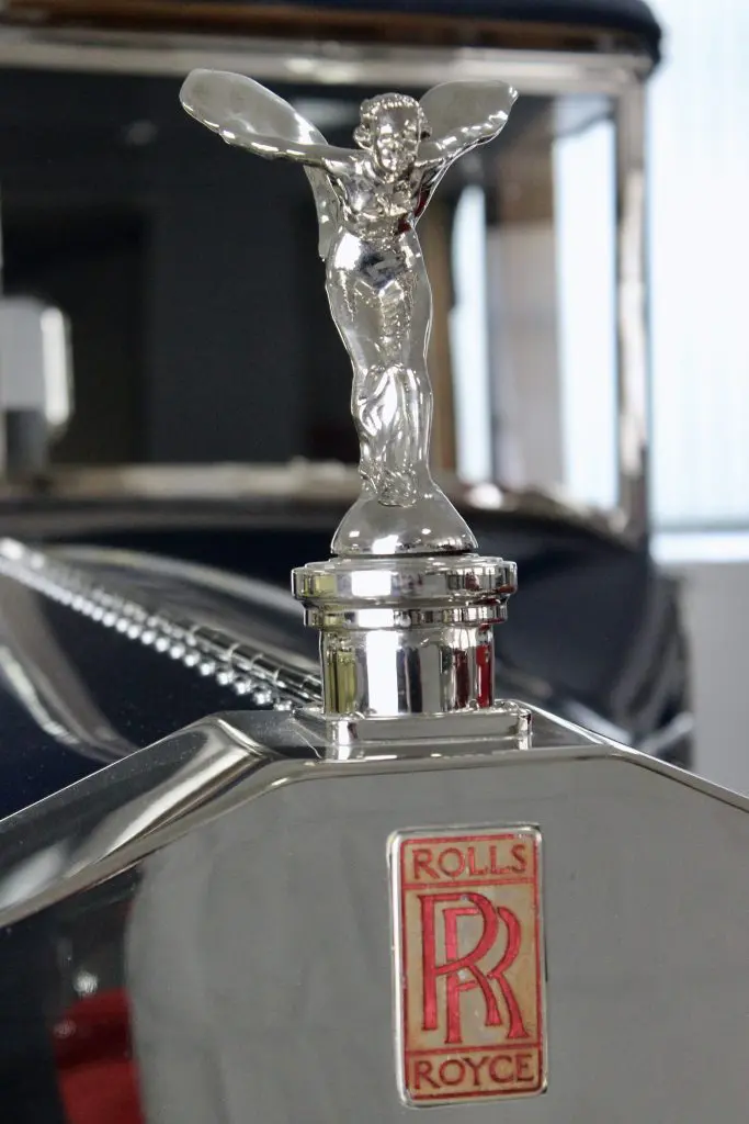 Close up of the silver mascot and red Rs logo of an old Rolls-Royce.