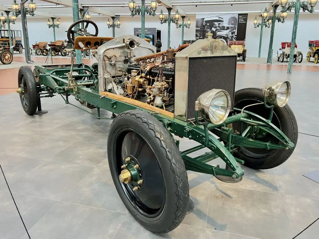 A Rolls-Royce chassis (without the coachwork) at the Musée National de l'Automobile, Collection Schlumpf. We can see the wheel and engine mounted on the metal chassis as well as the radiator grille, Rolls-Royce red logo and headlamps, but the body of the vehicle is missing.