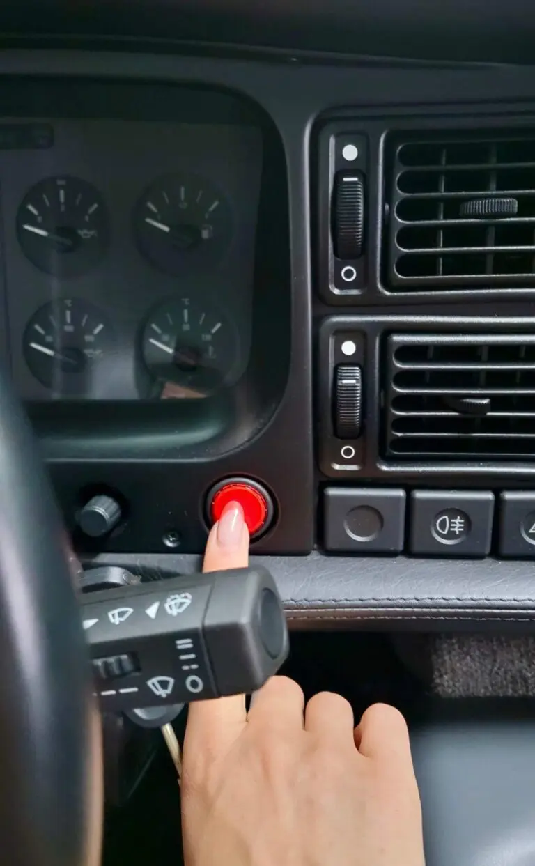 Start Button A manicured finger presses a red button behind a steering wheel