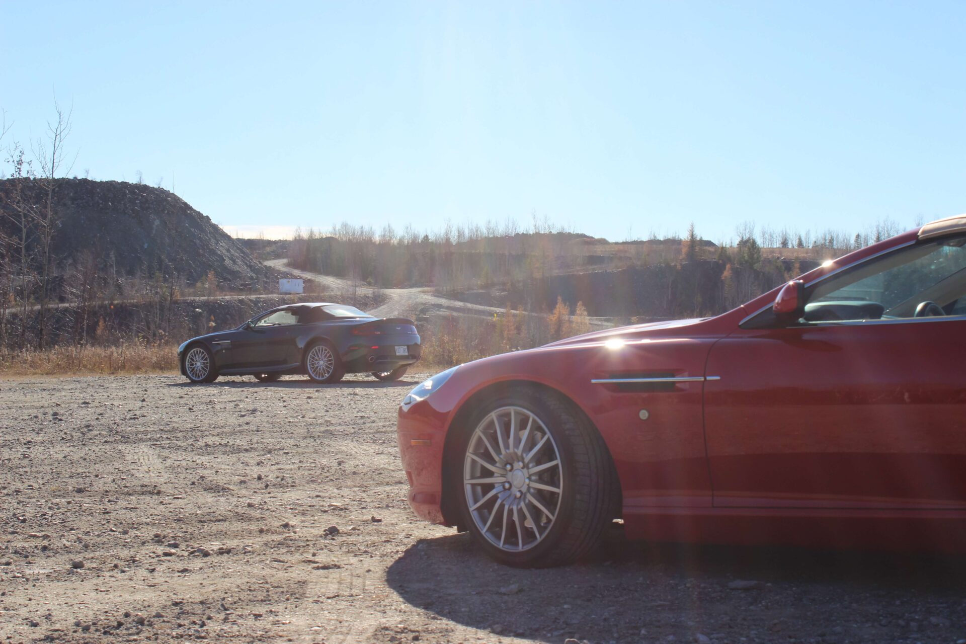 Aston Martin SB9 Volante in the forefront with another Aston Martin in the background. Both cars are on gravel