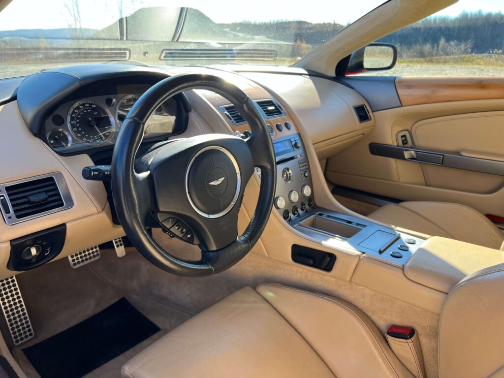 Interior of an Aston Martin SB9 Volante. Beige leather everywhere. The Aston Martin logo is clearly visible on the steering wheel.