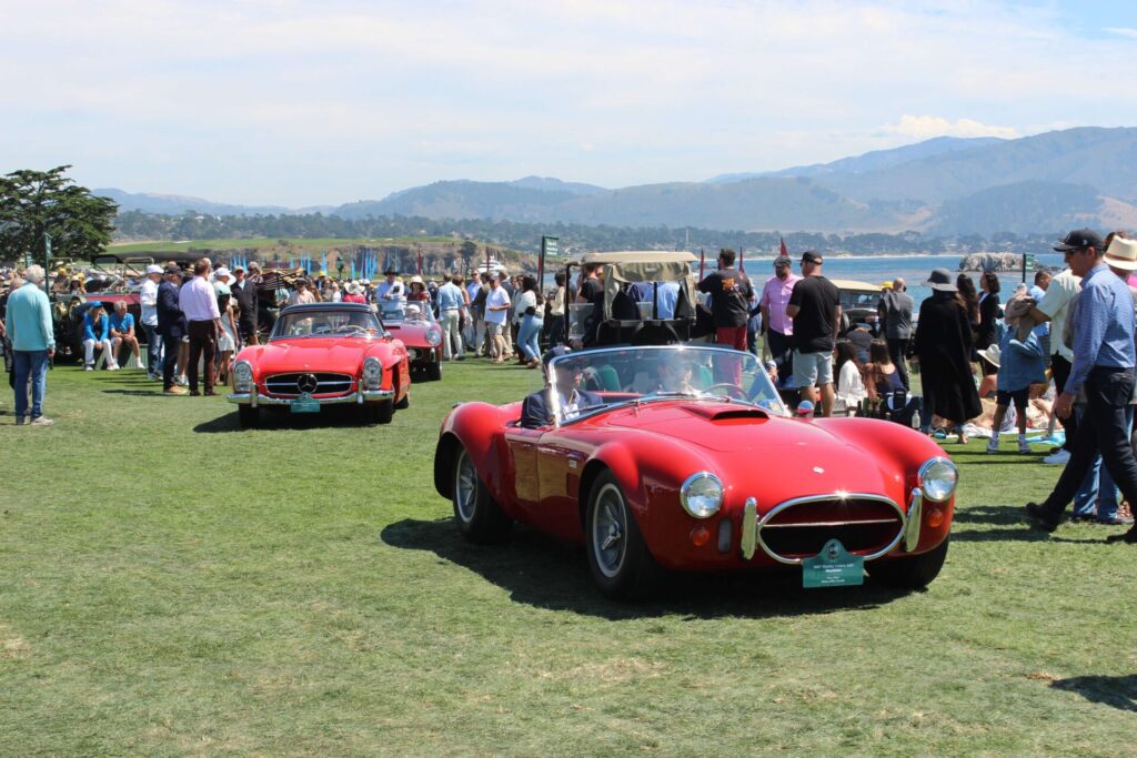 Tow red cars driving through the crowd at the Pebble Beach Concours d'Elegance 2023