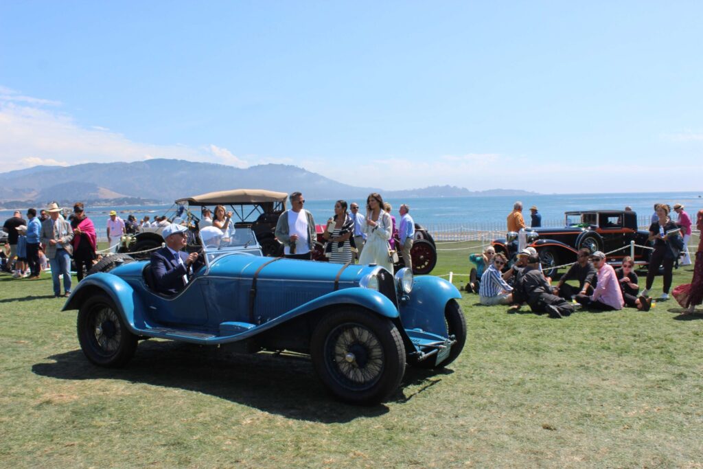 Blue car riding in crowd at the Pebble Beach Concours d'Elegance 2023