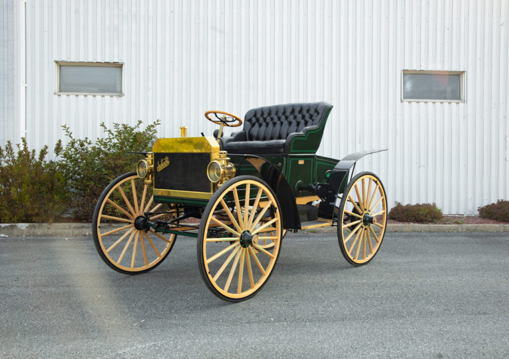 Early buggy-style vehicle with wooden-spoke high wheels and open-air seating area. The Schacht looks rudimentary.