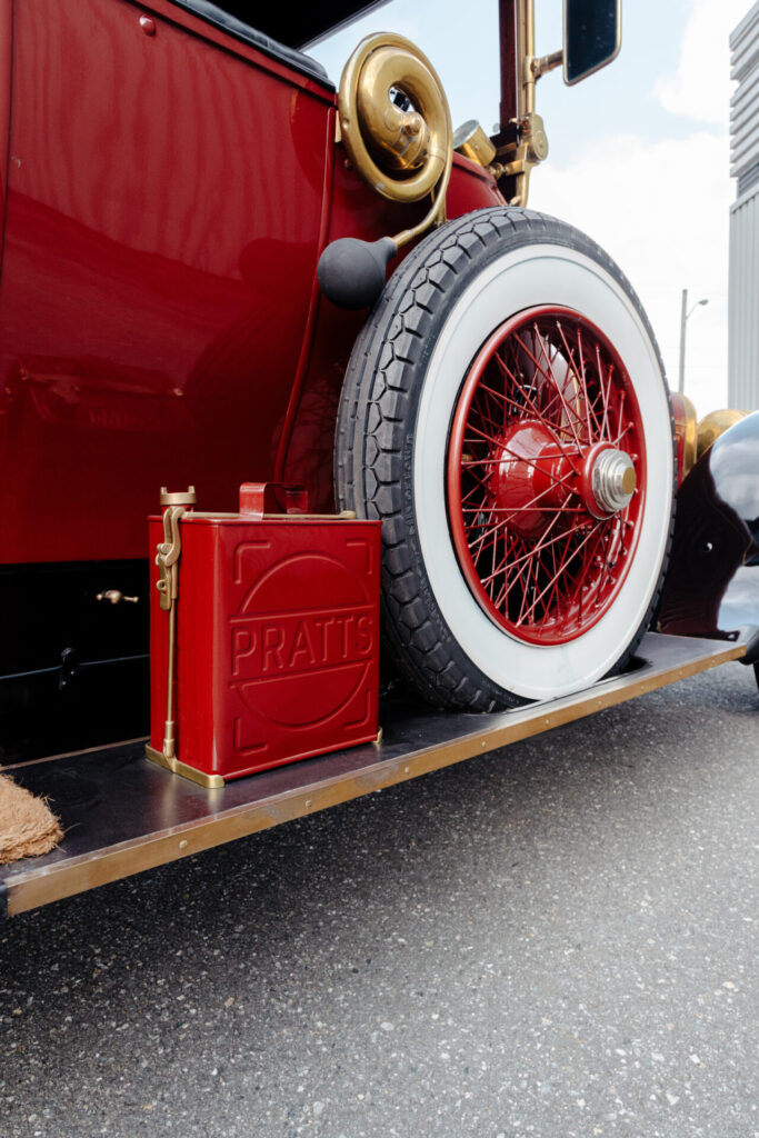 Un gros plan sur un bidon d'huile et une roue de secours d'une voiture de l'Ère du Bronze. La roue a des flancs blancs, et le bidon d'huile est de la même couleur que la voiture.