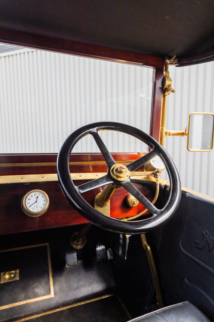 Close up of the steering wheel of a bronze era car. A clock is also visible on the dashboard.