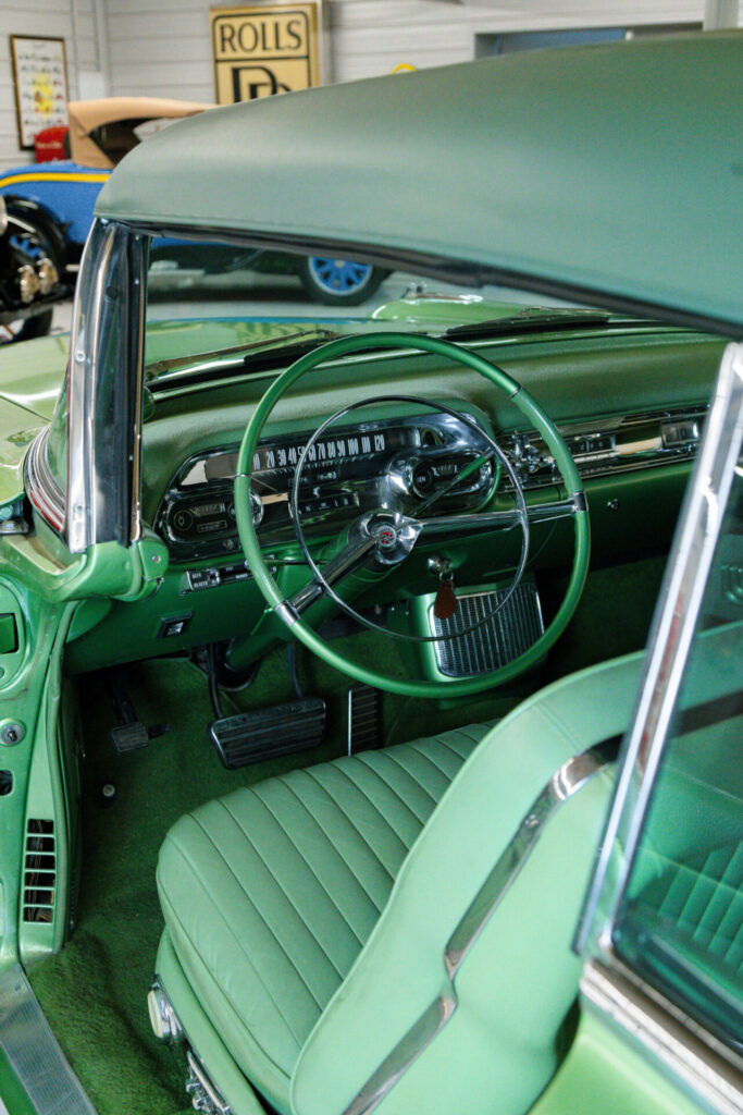 Intérieur luxueux en vert d'une Cadillac Eldorado Biarritz de 1957. La vue est depuis la porte du côté conducteur sous un angle supérieur. Du volant au tableau de bord, en passant par le cuir des sièges jusqu'aux tapis, tout est de la même teinte de vert.