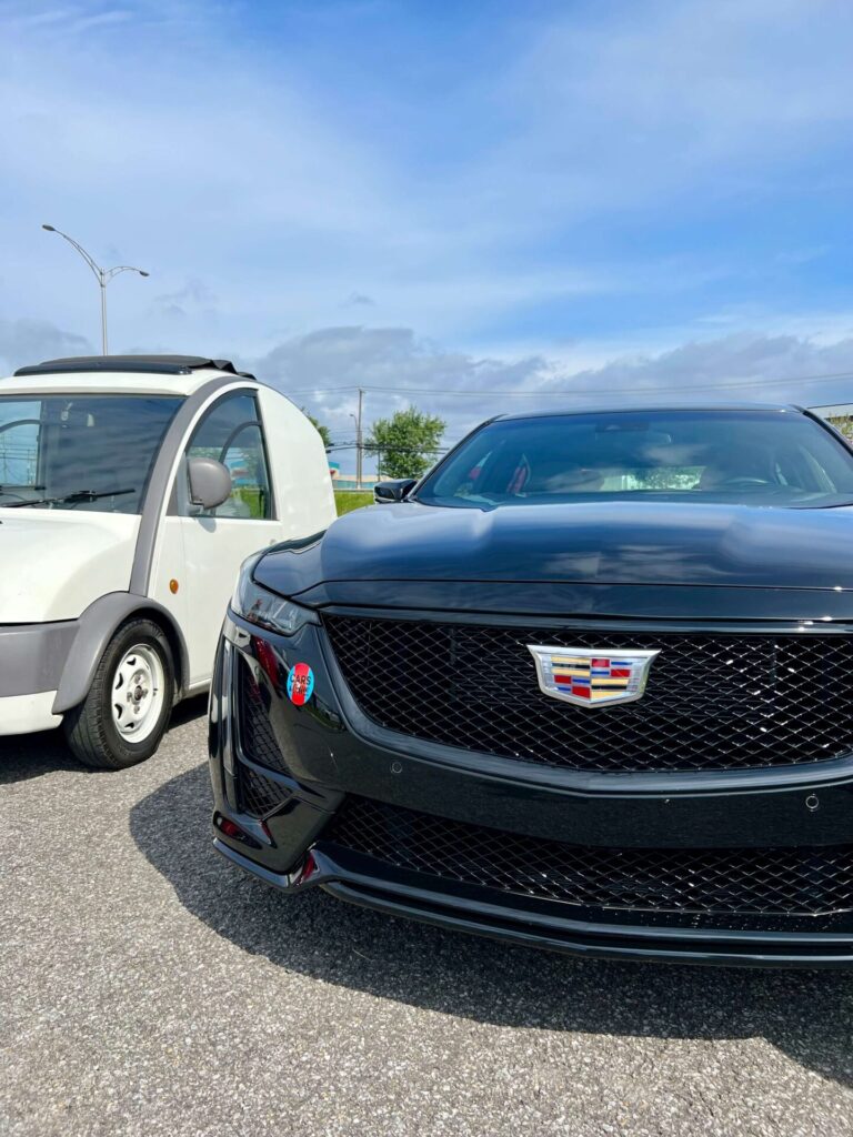 Plan rapproché de l'avant d'une voiture Cadillac noire stationnée à côté d'une petite voiture blanche