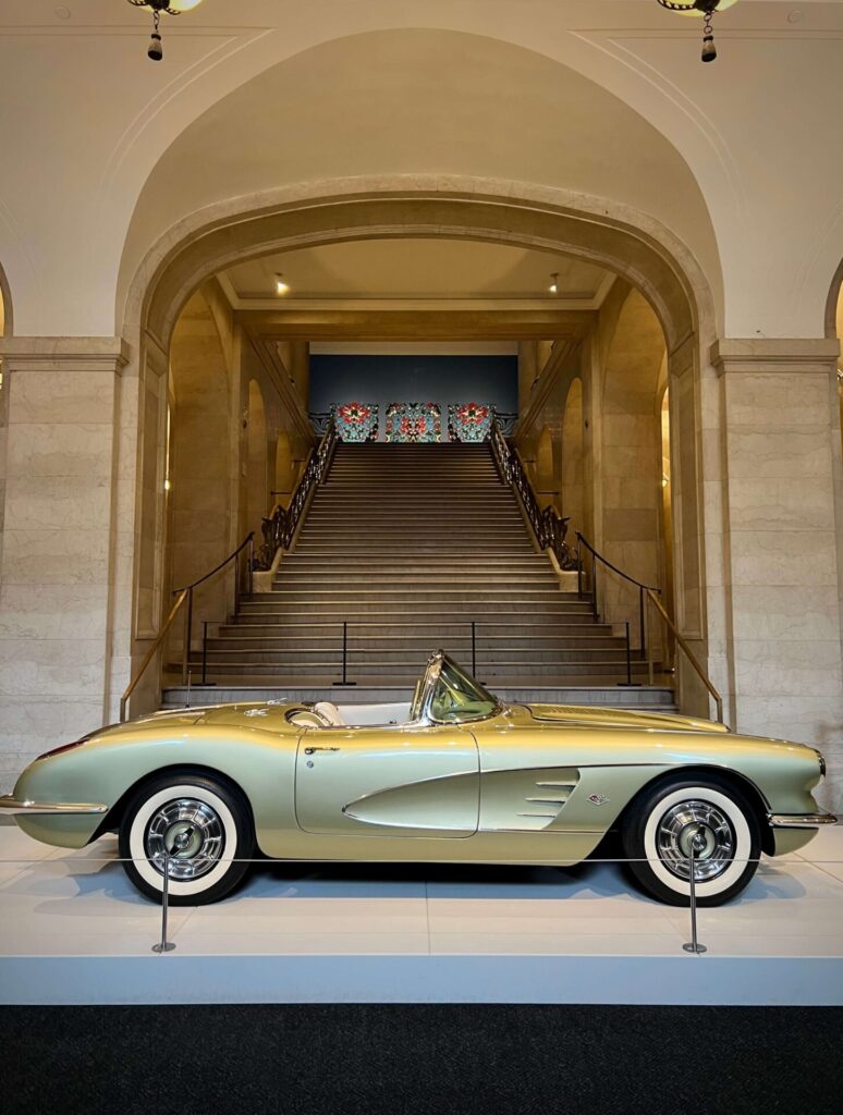 Corvette verte olive photographiée sur un podium au bas d'un grand escalier grandiose. Ruth Glennie a conçu cette Corvette spéciale pour General Motors en 1958."