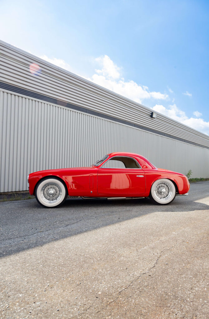 Vue de profil de l'Alfa Romeo 6C 2500. La voiture rouge au look sportif a des roues avec des flancs blancs.
