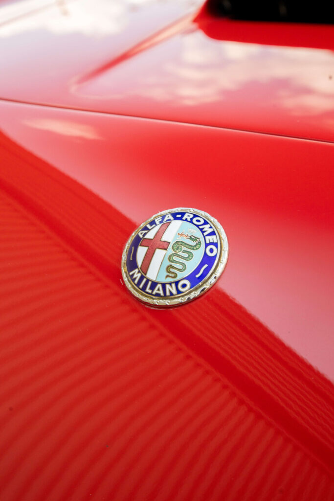 Un gros plan sur l'insigne d'Alfa Romeo sur une voiture rouge.