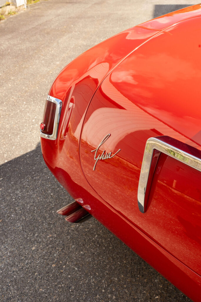 Badge Ghia calligraphié à l'arrière d'une voiture rouge.