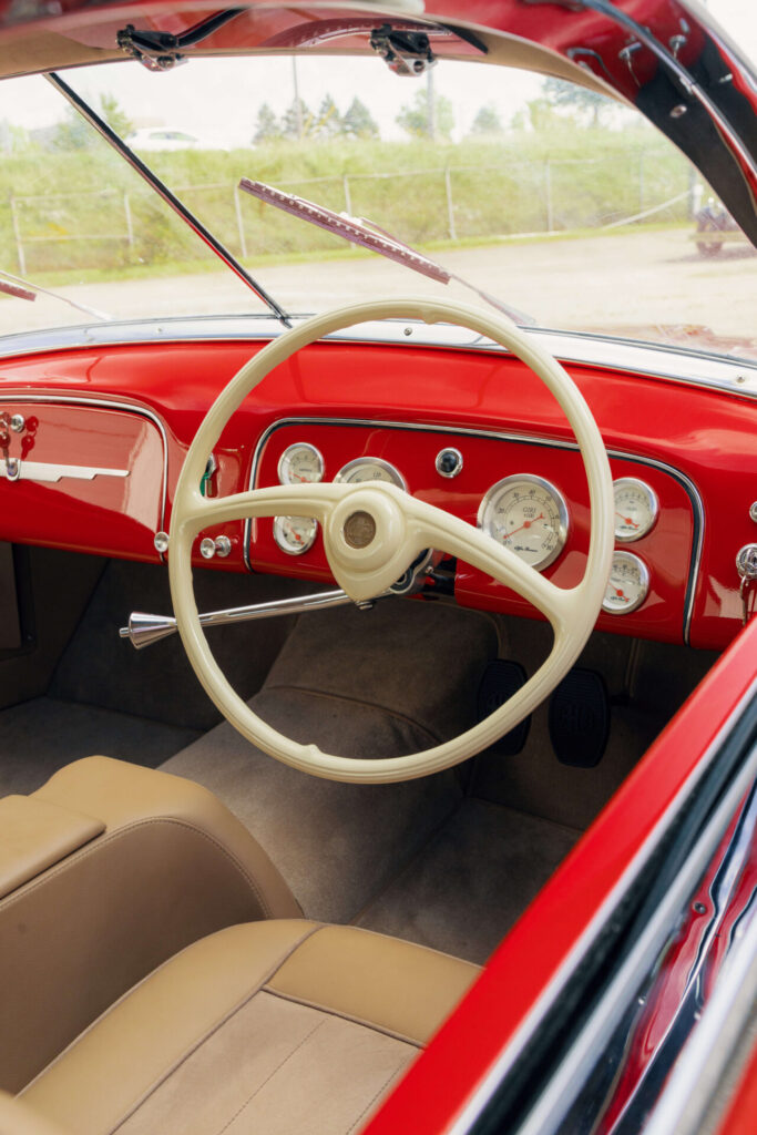 Vue de l'intérieur d'une voiture rouge. Le volant est plutôt fin et contraste avec le reste du tableau de bord.