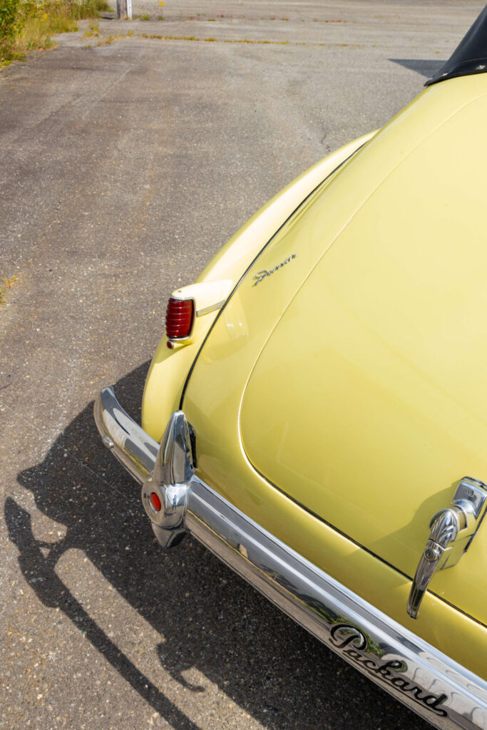 Extrémité arrière d'une voiture jaune disposée en angle de manière à donner l'impression d'un coin. Un badge métallique portant le nom "Darrin" est visible.