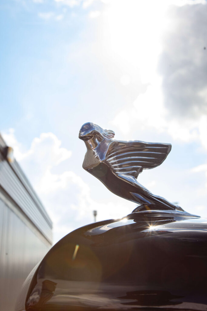 Close up of the flying lady mascot of a black Cadillac. The mascot is a metal statue of a woman with wings for arms leaning into the wind.