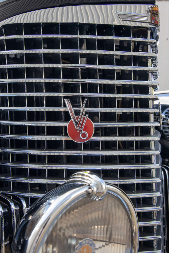 "V16" on a red circle is the metal badge seen on a metal car grille. The Cadillac V16 was a halo car and its impressive engine was clearly advertised on the car through badging.