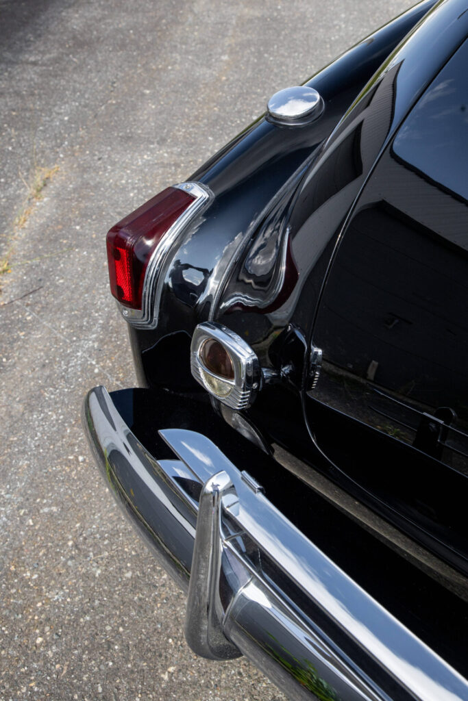 Red taillight of a black car with a chrome bumper.