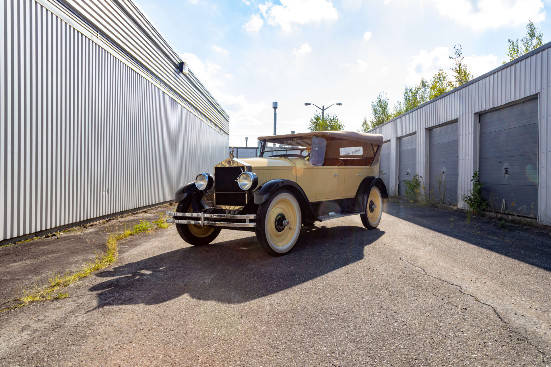 A yellow Moon Car on asphalt with garage doors and a bare grey wall in perspective. The car has a fabric roof and black accents.