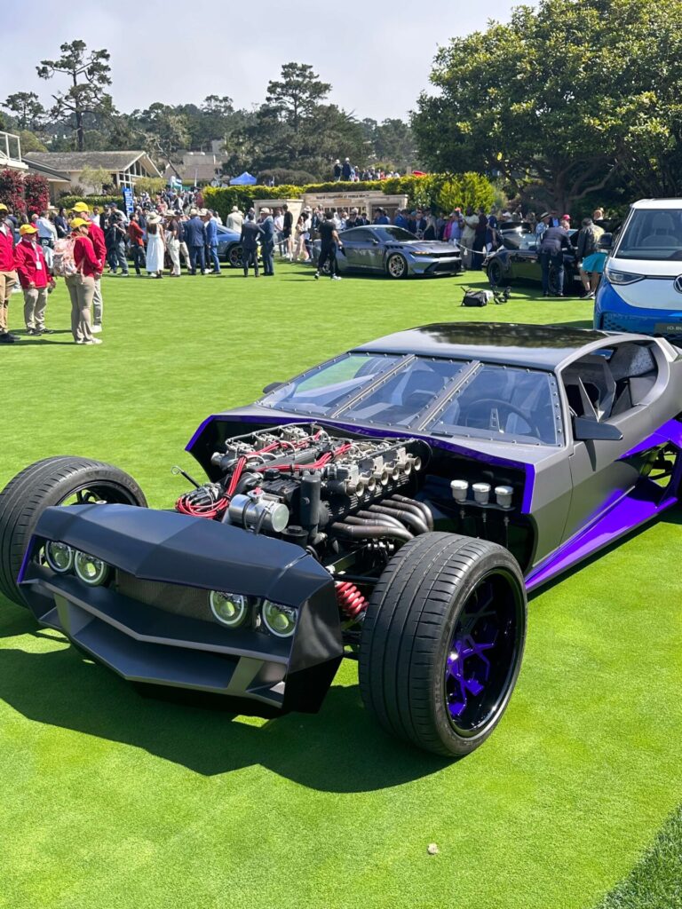 Hot rod version of an Espada. the car is dark grey and purple and is pictured on a bright green grass. The engine is exposed.