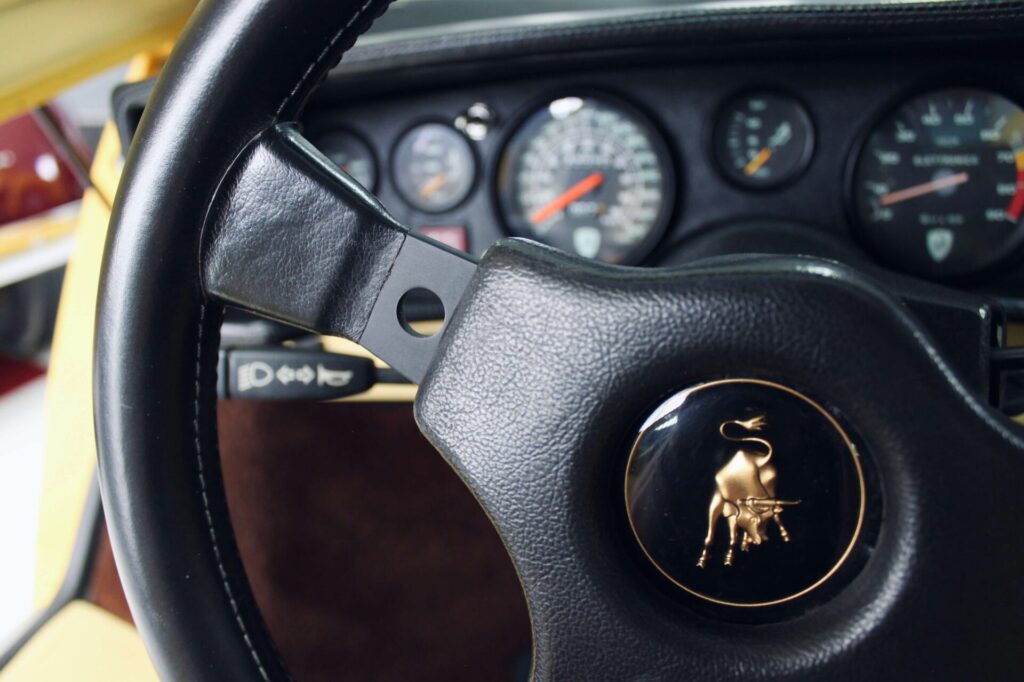 Image en gros plan du volant d'une Lamborghini Countach. Le logo du taureau en charge est représenté au centre du volant en plastique noir.