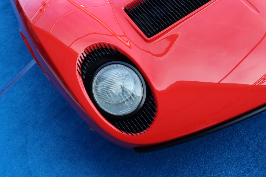 
Image en forme de coin de la lumière avant d'une Lamborghini Miura rouge sur un tapis bleu. La Miura est une voiture emblématique créée par Ferruccio Lamborghini.