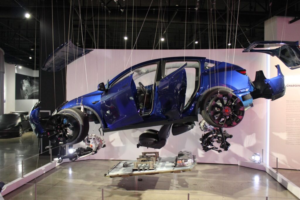 A Tesla car is suspended in the air by strings and all of its parts are detached from one another.