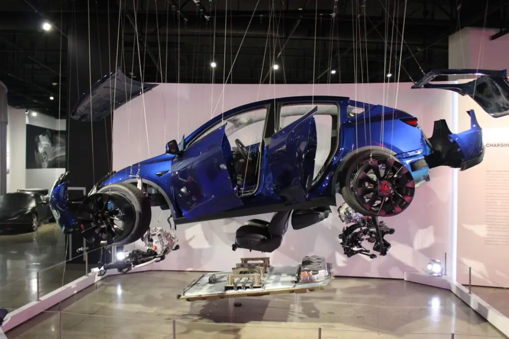 Une voiture Tesla est suspendue dans l'air par des cordes, et toutes ses pièces sont détachées les unes des autres.
