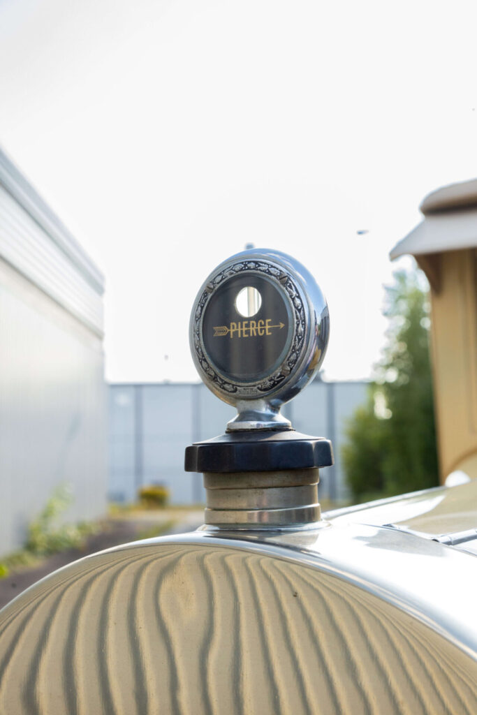 Closer look at a MotorMeter on the radiator cap of a yellow car. The words "Pierce" are written on it.