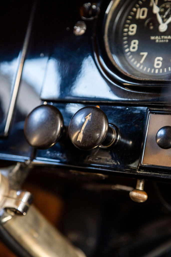 Small arrow pointing up painted on a black button on the dashboard of a car.