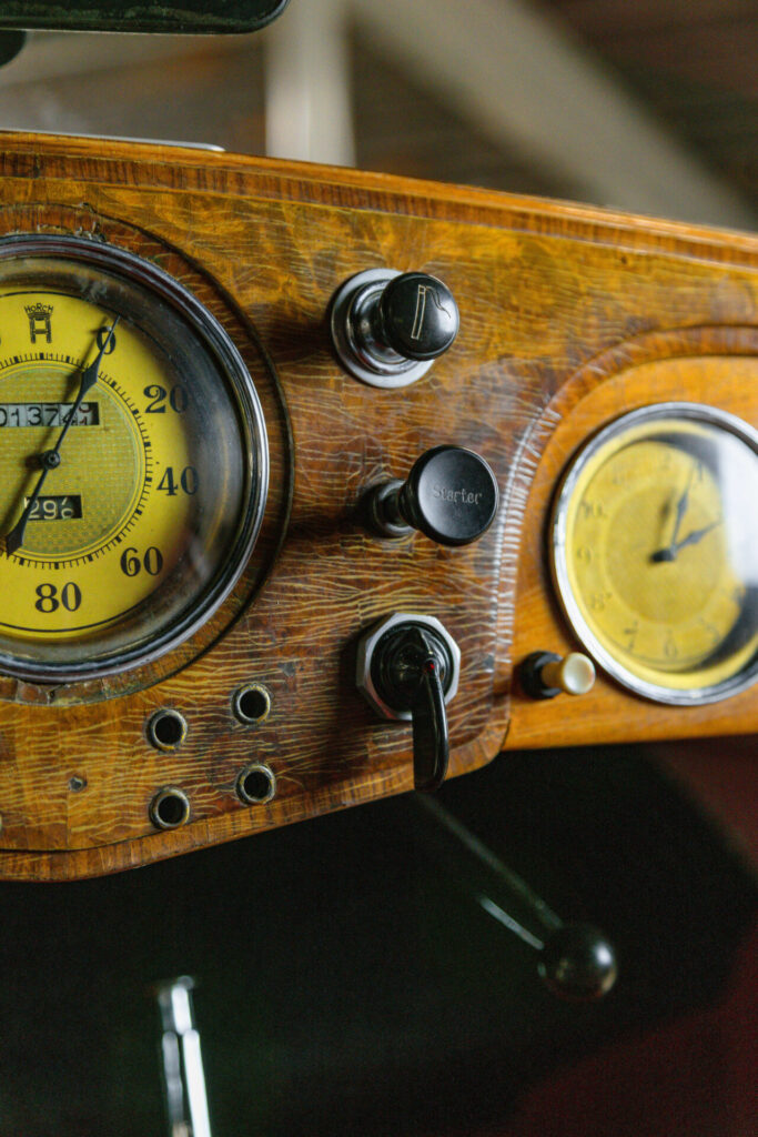 Close up of a wooden dashboard with two dials and three other levers.