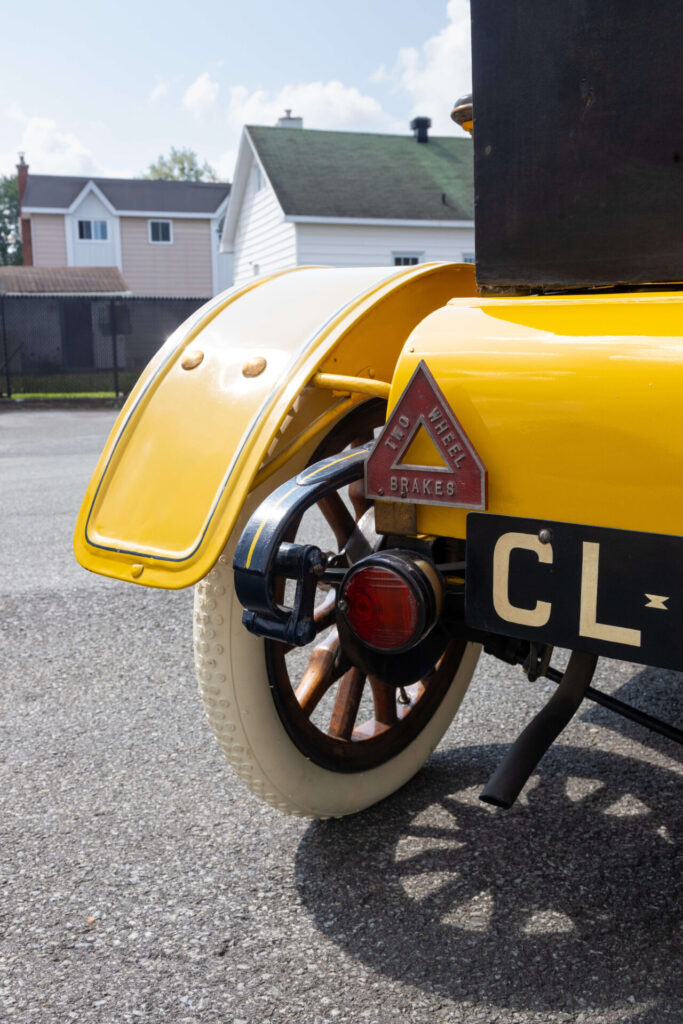 Vue rapprochée du quart arrière d'une voiture jaune avec des pneus en caoutchouc blanc sur des roues à rayons en bois.