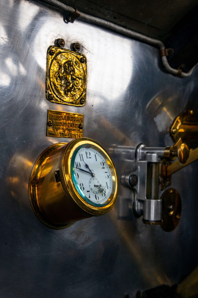 Une petite horloge dans un contenant en laiton sur un tableau de bord en métal. D'autres détails en laiton sont également visibles dans le cadre de la photo.