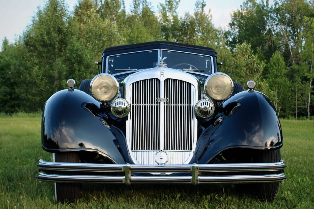 Horch 853. Black and grey classic car viewed from the front on grass with trees in the background. The car has a silver-coloured angled grille, the windshield is divided in two sections and the convertible top is black. The "auto union" logo is visible at the center of the grille.