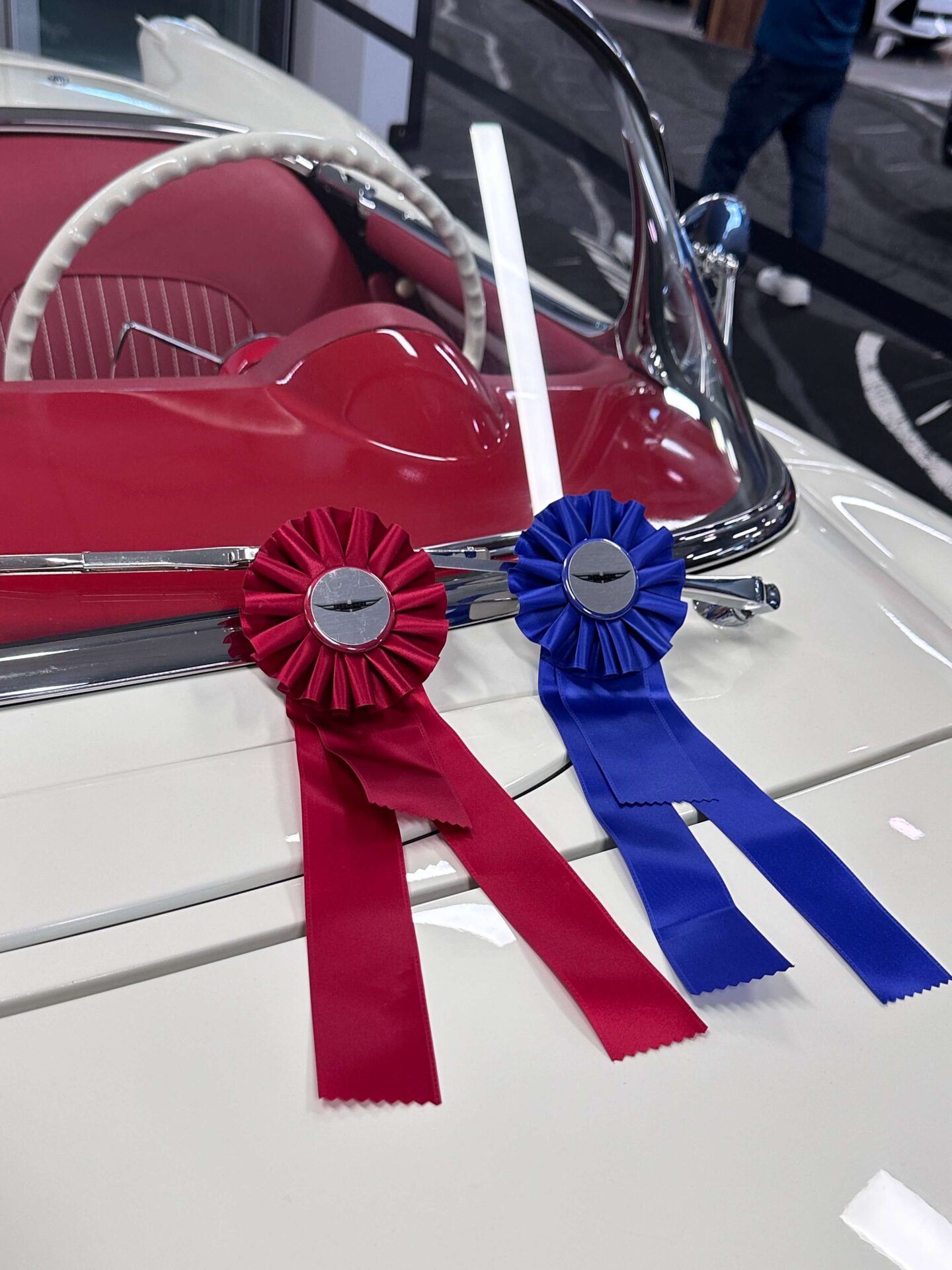 A red and a blue ribbon attached to the windshield wiper of a white car with a red interior.