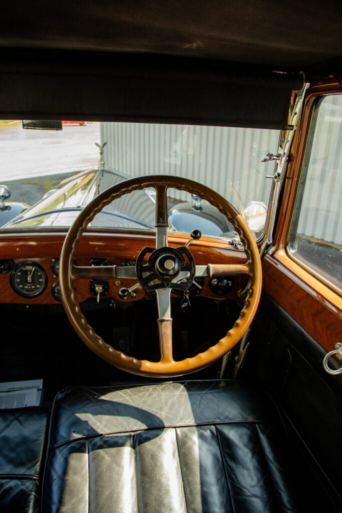 Close up of the wooden steering wheel of a Rolls-Royce from 1928. The wooden dashboard as well as the mascot of the car are also visible.