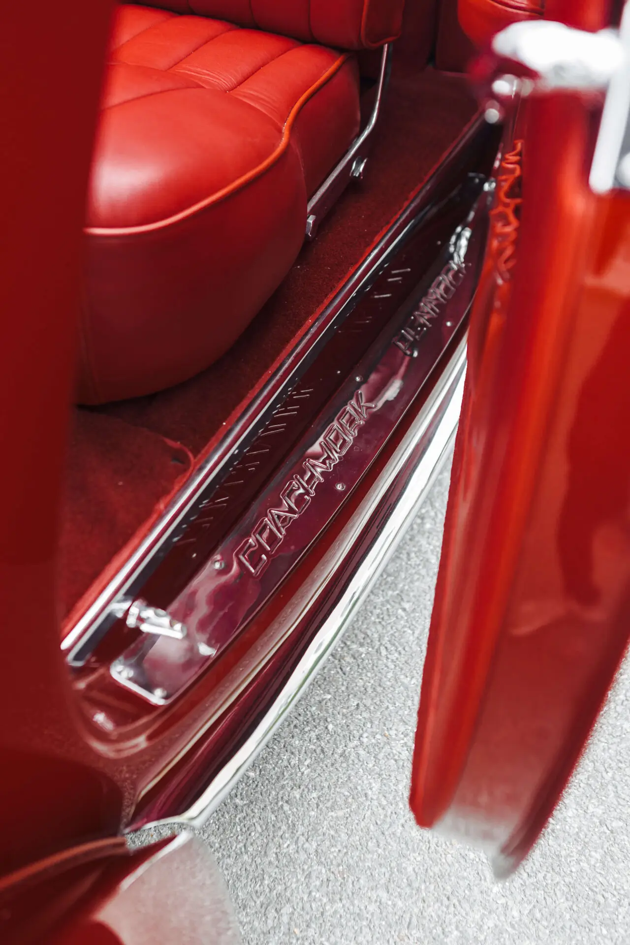 A close up of an open door of a red car with red leather seat. We can see the word "Pennock" on the metal frame of the door. Pennock is a Coachbuilder