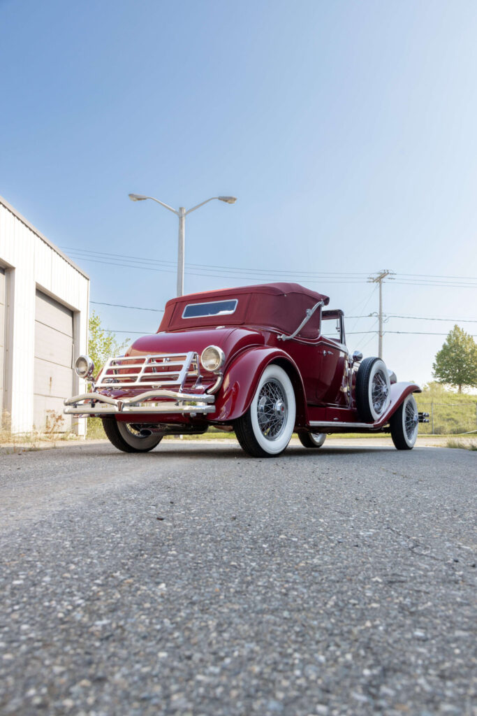 Vue arrière et en angle d'une Duesenberg Model J rouge. Un porte-bagages est visible à l'arrière de la voiture. La voiture est photographiée sur de l'asphalte.