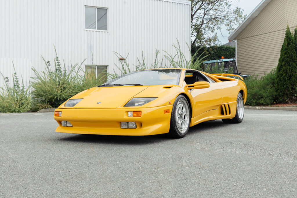 Une Lamborghini Diablo jaune de 1992 photographiée en angle devant un bâtiment blanc et quelques buissons.