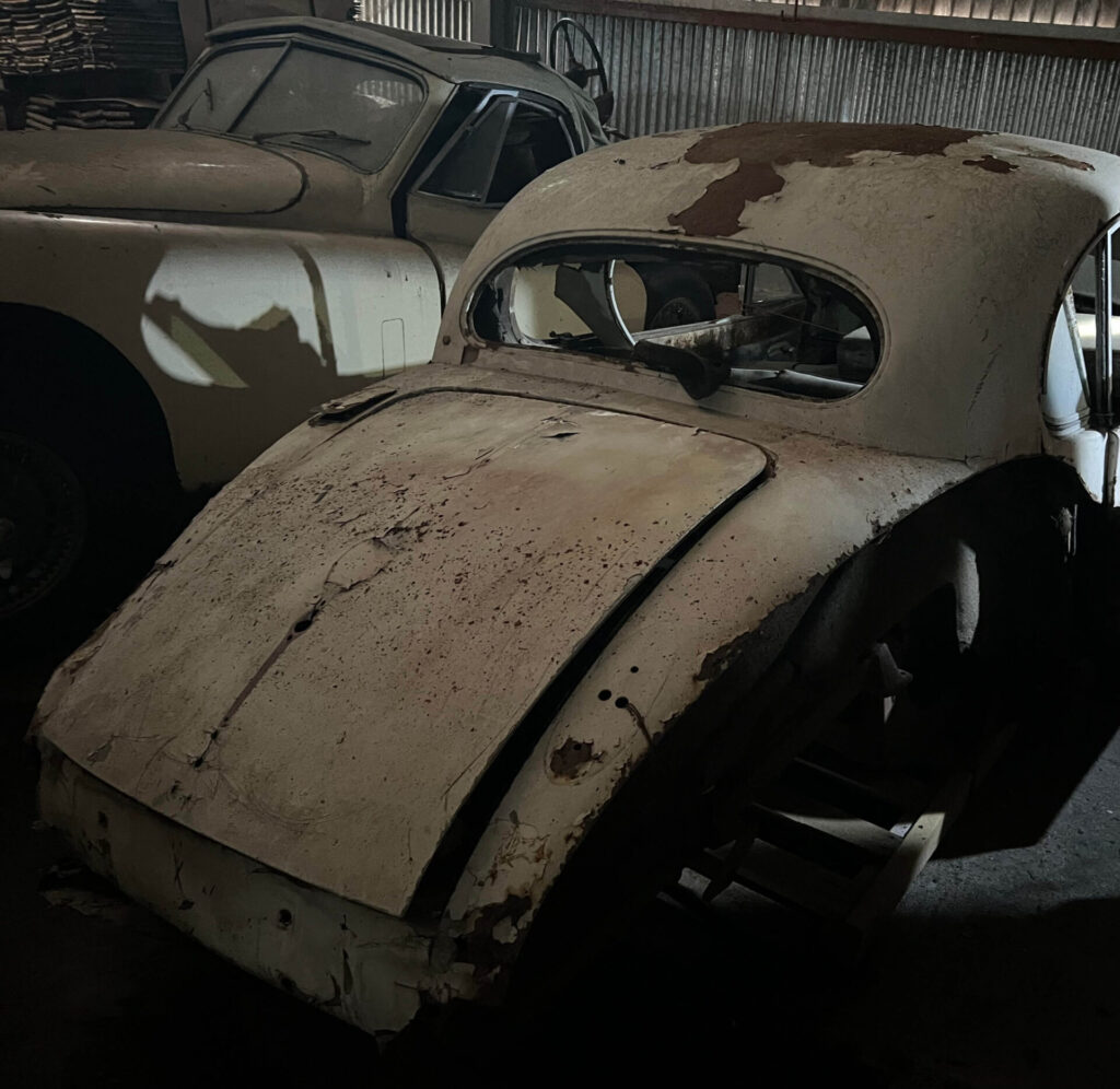 Two broken down cars in a barn. The metal of the cars looks old, rusted and chipped.