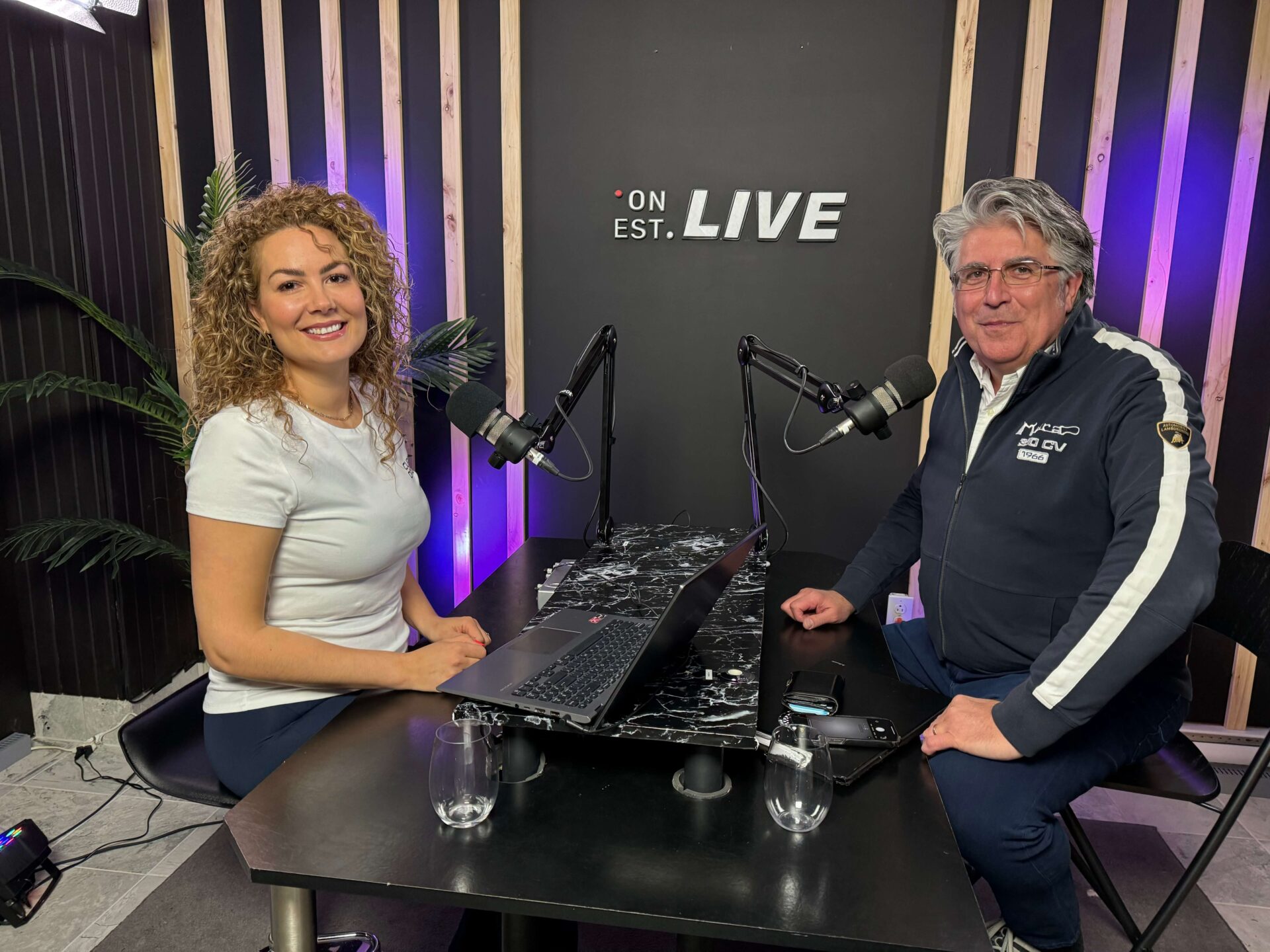 Une femme et un homme sont assis à une table dans un studio d'enregistrement de podcast. Ils ont tous les deux un micro.