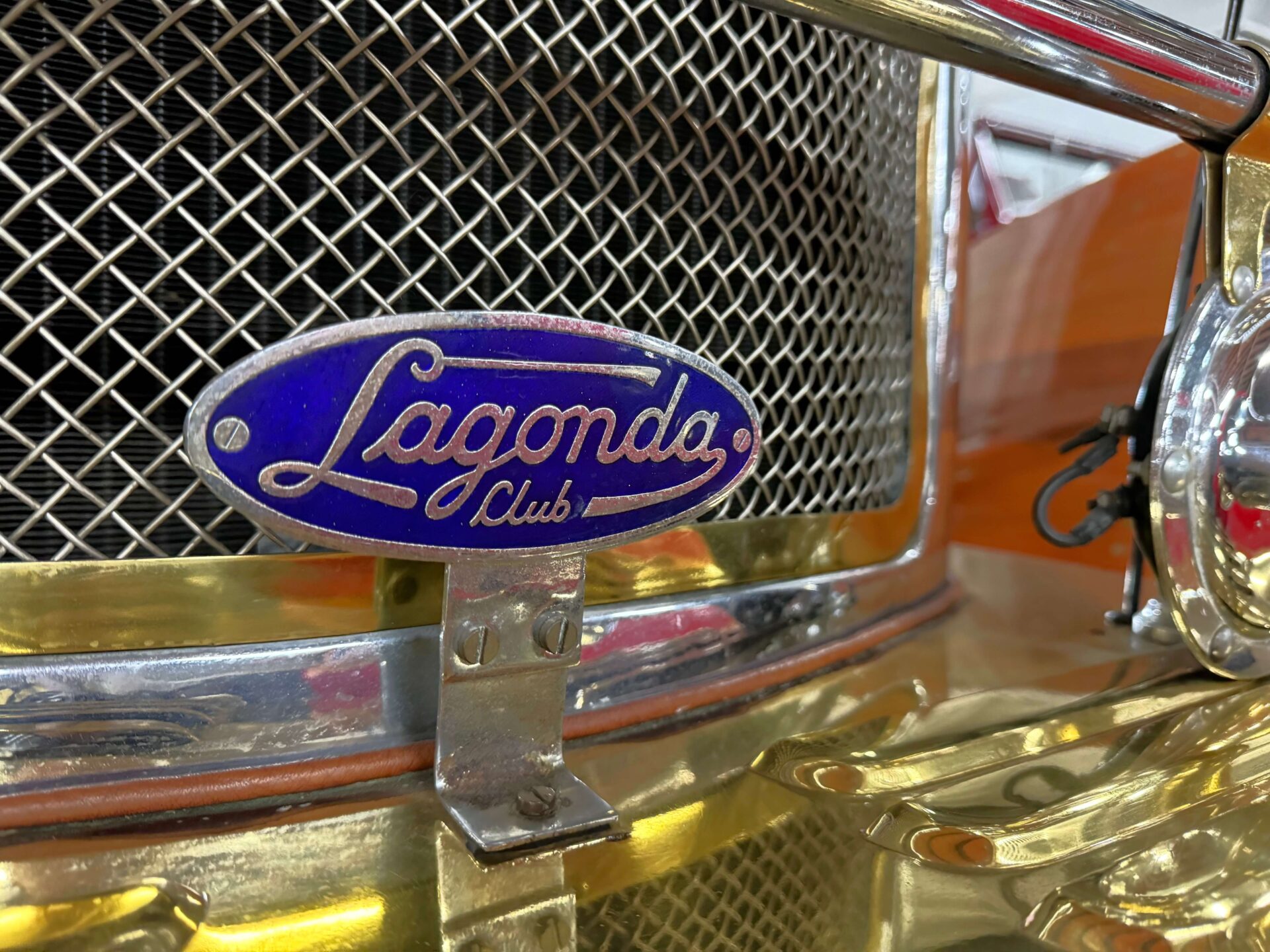 Close up at the badge of the Lagonda Club installed on a car. The badge is simple the name of the club written on a blue background on an oval badge.